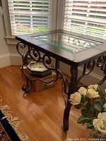 Side view of the table showing wrought iron legs with scrollwork and wooden top with glass insert.
