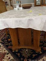 Close-up photo of the fluted pedestal base of the Thomasville oval dining table with a white tablecloth partially covering the top.