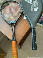 Wilson Super Power and Pro Kennex junior oversize tennis rackets side by side on wooden table, Wilson showing red 'W' logo on strings
