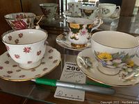 Photo of four porcelain tea cups and matching saucers on a glass surface, showing various floral patterns and gold trim.