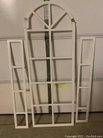 Full view of the large arched grid and two smaller rectangular white plastic window grids leaning against a garage door.