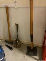 Photo of four tools leaning against wall including wedge axe, shovel, sod packer, and wedge splitter axe head, showing overall lot contents.