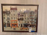 Framed artwork showing a cityscape with buildings, people and signage, in a vintage impressionist style, featuring muted pastel colors.