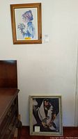View showing two framed artworks: upper wood framed limited edition print of girl with flowers, lower ornate framed religious artwork.