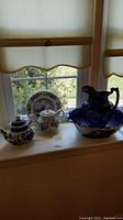 Full view of teapots, pitcher with basin, and plate on window sill under light