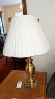 Front view of the brass lamp with white pleated fabric shade placed on a wooden table.