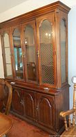 Full view of the 8 door wood and glass china hutch showing upper glass paneled doors with lattice design and lower solid wood doors.