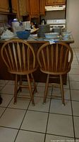 Two wooden counter stools with spindle backs placed side by side on tiled floor in kitchen environment.