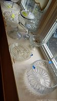 Seven clear glass cut and pressed glass dishes including tiered server and pedestal bowls lined on window sill