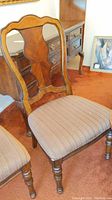 Photo of wooden dining chair with striped fabric seat and curved carved backrest near matching furniture.