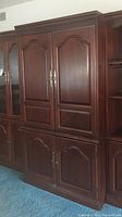 Close view of upper and lower cabinet doors with brass handles on wooden entertainment armoire