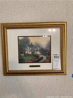 Framed Thomas Kinkade artwork showing a home surrounded by a garden, with gold frame and glass protecting the artwork.