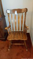 Full frontal view of wooden rocking chair showing vertical carved back slats, armrests, and rockers on bottom.