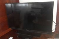 Samsung 32-inch flat screen TV showing the full front view including stand, screen off and reflecting surroundings.