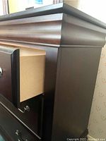 Close-up of dresser corner showing drawer pulled open with light wood interior and silver round knob.