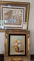 Two framed wall art pieces stacked on a couch: upper piece is a sepia-tone ballet print with a ballerina in blue tutu titled "Someday", lower piece is a floral painting in a gilt frame.