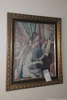 Full view of one framed wall art piece depicting two women at a piano, showing gold-tone carved frame.