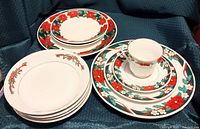 Photo showing the full 11-piece set of poinsettia-themed dinnerware including plates, bowls, cup, and saucer arranged on dark fabric.