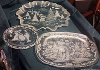 Three crystal platters displayed on dark fabric showing winter scene engravings.