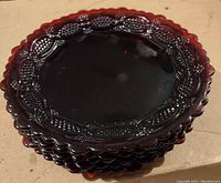 Stack of five red glass dessert plates showing the scalloped edge and decorative patterned rims.