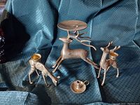 Photo showing four brass deer candleholders along with a brass chamber candleholder, arranged on a textured blue fabric.