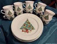 Photo showing 10 white china mugs and 4 dinner plates each decorated with a colorful Christmas tree design including ornaments, lights, and a red train toy.