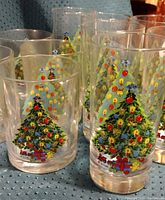 Close-up of several glass tumblers showing detailed Christmas tree ornament and gift decorations on transparent glass.