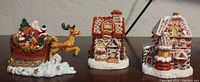 Front view of three Christmas village buildings including Santa on sleigh and two gingerbread houses.