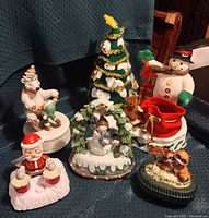 Wide view of entire musical Christmas decor lot showing all seven figurines arranged together on a blue fabric background.