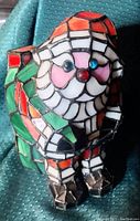 Close-up view of Tiffany style stained glass lampshade shaped like Santa Claus, showing colors and details of glass pieces and metal framing.