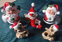 Photo showing all five ceramic figurines including Santas, elf, and two animals with Santa hats on a blue quilted surface.