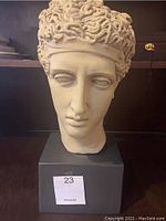 Front view of the beige Caesar bust sculpture with curly hair, placed on a black pedestal base.