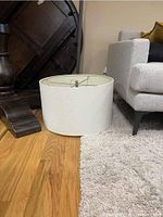 Side view of the white hanging drum lamp shade placed on hardwood floor near sofa and table base.