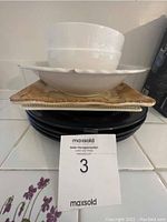 Stack of dishes including black plates, white square plates with a floral pattern, white round bowls, and one large white salad bowl on top.