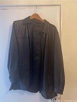Front view of black leather jacket on hanger, showing button closure and collar.