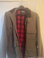 Front view of the medium men's fall jacket by Polo Ralph Lauren in brown with flap pockets and corduroy collar, showing red and black buffalo plaid lining inside.