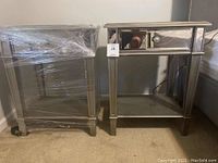 Pair of mirrored night tables side by side; left table wrapped in plastic, right table unwrapped showing drawer and shelf