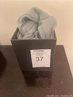 Soft folded light spruce green scarf inside a dark box labeled MaxSold