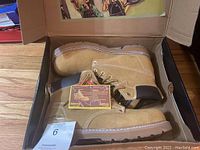 Two images showing a pair of tan steel toe work boots in original box with tags, size label is not clearly visible for size 11 match but seller states size 11.