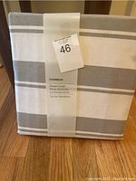 Photo of the packaged Crate and Barrel shower curtain showing folded fabric with gray and white stripes and label indicating size and brand.