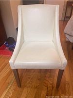 Front view of white leather upholstered chair with wooden legs on hardwood floor.