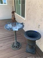 Metal bird bath with a round, shallow basin decorated with a metal windmill and bird figures on top, standing on an ornate pedestal base.