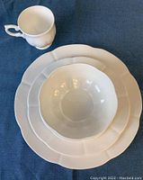White bone china teacup, soup bowl, salad plate, and dinner plate on blue fabric background showing scalloped edges.