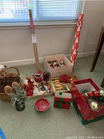 Photo showing Christmas decorations arranged on floor including a bear basket, small tree, candy dish, wrapped gift boxes, candy cane decorations, and boxes of ornaments.