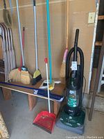 Photo showing all cleaning tools together including broom handles, dustpans, and vacuum.