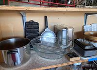 Shelf with large stainless steel pot, glass Pyrex dishes, metal fish grill pan, and other utensils