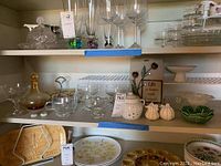 Full view of shelves showing glassware, plates, decanter, garlic crock, salt and pepper shakers, green leaf dish.