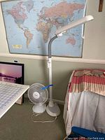 Full view of the standing LED lamp and small oscillating fan next to a bed with a map in the background.