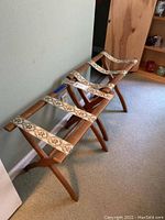 Two vintage wooden luggage racks placed side by side against a wall, showing the fabric straps and wood finish.