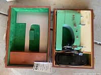 Top view of Bell mini sewing machine in wooden case with green interior padding and black foot pedal.